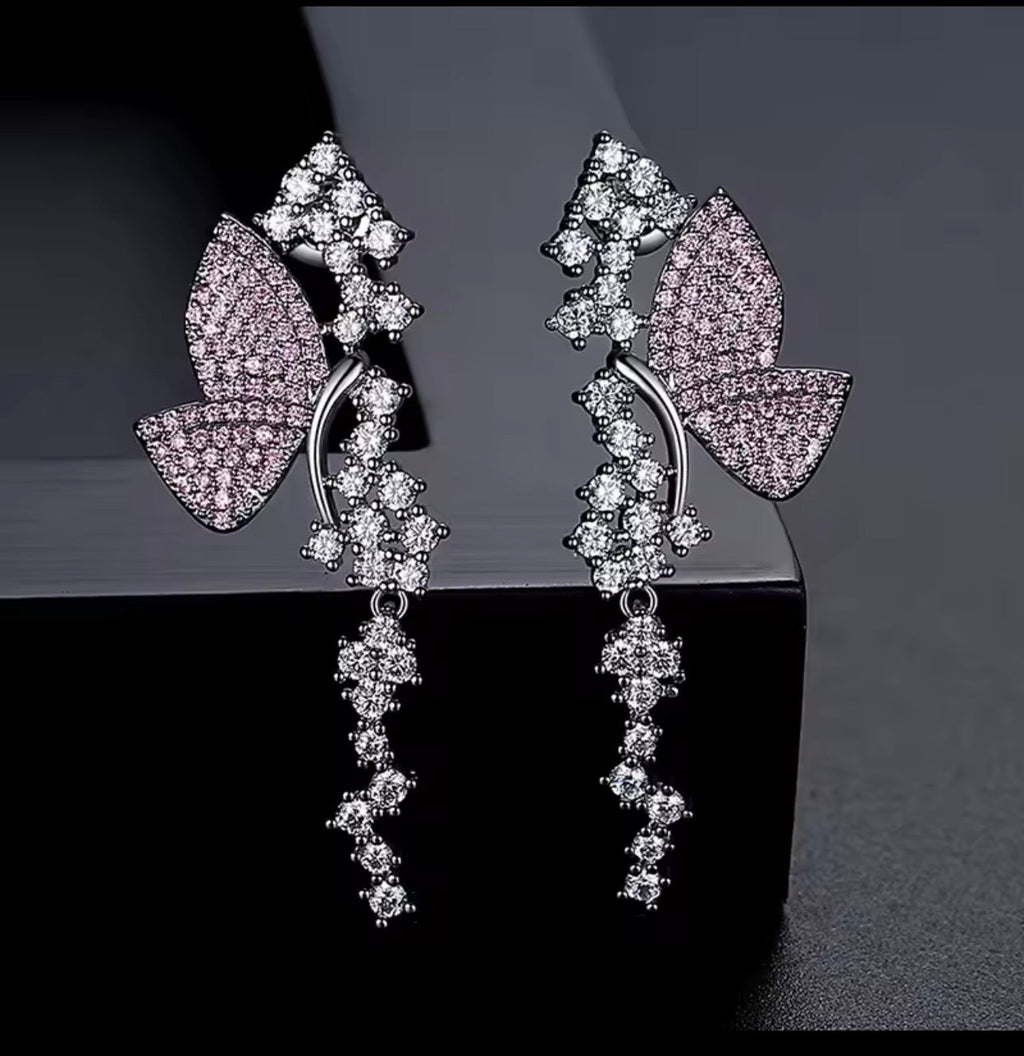 Pink pavé butterfly dangle earrings on a dark background