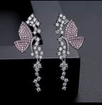 Pink pavé butterfly dangle earrings on a dark background