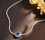 Blue sapphire halo tennis necklace styled on a dark surface